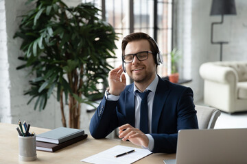 Obraz premium Happy male CEO or boss sit relax at office desk listen to music in modern headphones. Smiling young Caucasian businessman in earphones enjoy good quality sound on gadget. Technology concept.