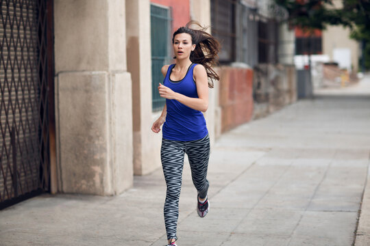 Determined sportswoman running on sidewalk