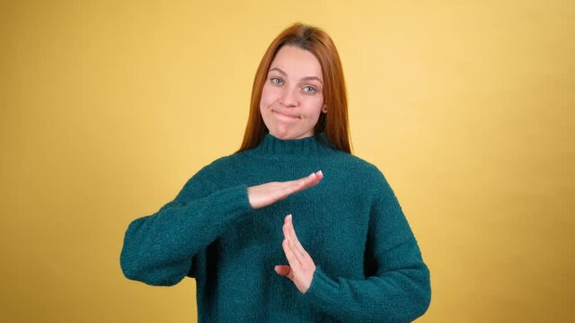 Tired young woman looking with pleading frightened eyes and showing time out hands gesture, asking for break, needs pause and rest. indoor isolated on yellow background