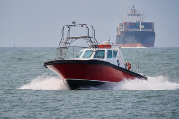 Naklejka premium Schnell fahrendes Lotsenboot mit Container Schiff im Hintergrund