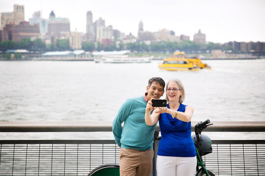 Happy mature couple taking selfie while standing on promenade by river in city