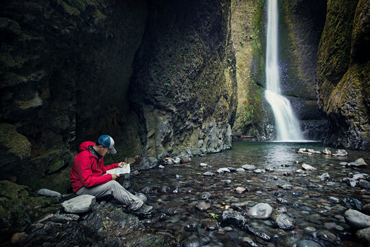 Man reading map while sitting by waterfall in forest