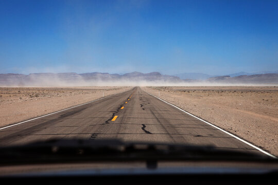 Road amidst field against clear blue sky seen through vehicle windshield