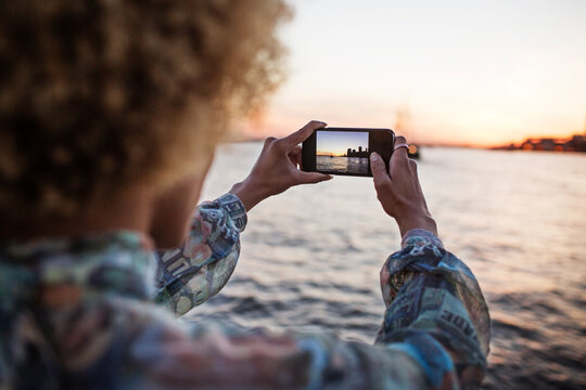 Cropped image of woman photographing sea through smart phone