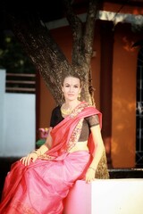 A girl in a sari sits by a tree in an Indian temple