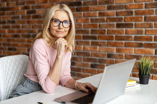 Beautiful mature businesswoman working with laptop,looking at the camera, smiling and typing, interrupted from work,best worker,workoholic,beautiful neat middle-aged woman,working at the modern office