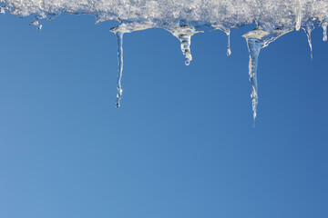 Topniejące sople lodowe na zadaszeniu budynku zimą. 