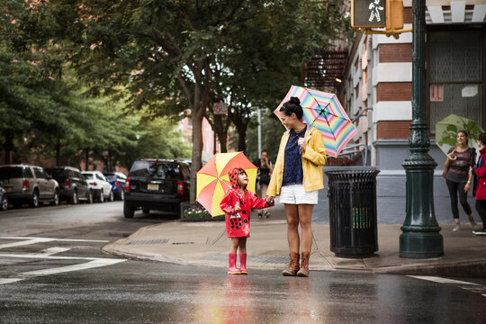 Mother and daughter looking at each other while holding umbrellas on street