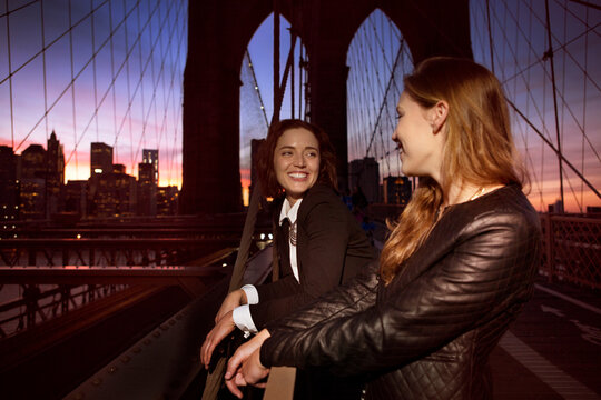 Cheerful friends looking at each other while standing on Brooklyn bridge