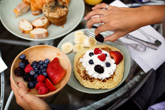 Cropped image of hands garnishing pancake with fruits and whipped cream on table