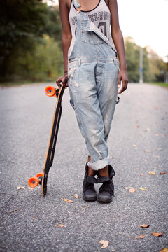 Low section of woman holding skateboard standing on street