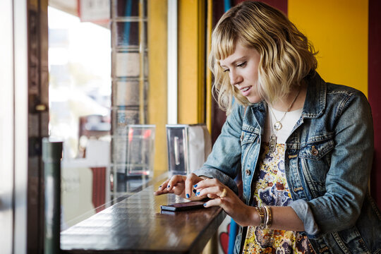 Woman using smart phone by window in cafe