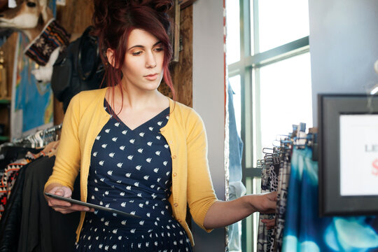 Female owner with tablet computer counting clothes in clothing store