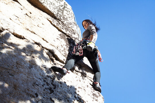 Low angle view of woman rock climbing against clear blue sky