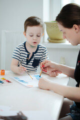 mom with a child in quarantine draws colorful paints  at a white table