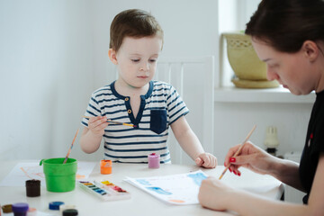 Child and his mother paint with paints at the table in the apartment while in isolation in quarantine