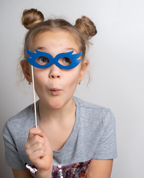 Little girl with wondered facial expression in paper eyeglasses masquerade mask studio portrait. Amazed female child with surprise on face. Overjoyed kid wearing beautiful masque. Carnival costume