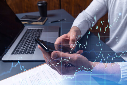 Trader holding in the hands a smart phone and researching stock market to proceed right investment solutions. Internet trading and wealth management concept. Hologram Forex chart over close up shot.
