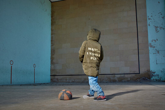 Boy with his hands in his pockets next to a deflated basketball ball.