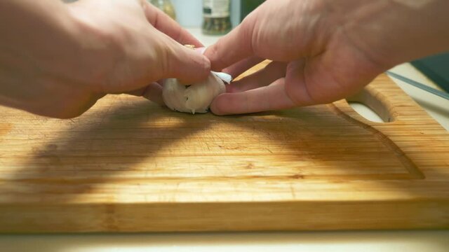 close-up of male hands chopping garlic on a wooden cutting board.