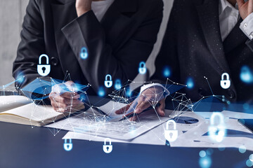 Two businesswomen working on the project to protect cyber security of international company. Padlock Hologram icons over the table with documents.