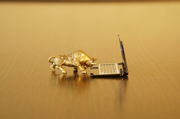 A metal bull with a laptop on a gold background.