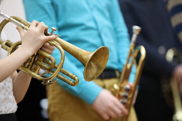 A child girl plays the trumpet holding an old shabby musical instrument in her hands and pressing the buttons with her fingers on the background of adult musicians. Solo