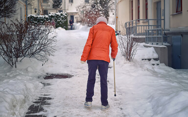 Disabled woman walks with stick after snowfall. Lame woman, disability and injury concept. Old...