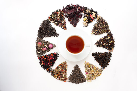 Different Types Of Tea And Herbal Mixtures With Berries Laid Out In A Circle Around A White Cup Of Tea On A White Background. Time To Drink Tea. View From Above. Healthy Drinks.