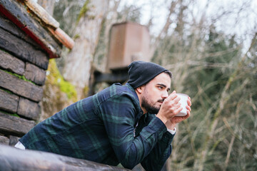 Hipster guy drinking coffee on the cottage terrace, melancholic autumn mood