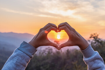 hands in shape of love heart sunset background