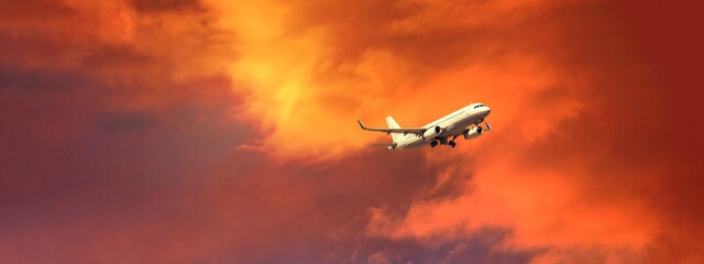 Ultra wide panoramic zoom photo of passenger airplane taking off at sunset with beautiful orange sky and clouds