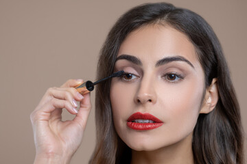 Focused brown-eyed woman applying mascara on eyelashes