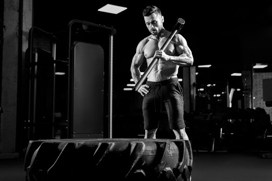 Muscular bodubuilder holding sledgehammer on shoulder.