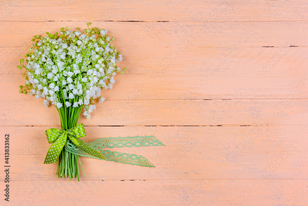 Wall mural bouquet of lily of the valley flowers with a bow and ribbon on a wooden pink background with a copy space - Wall murals
