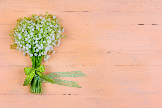 bouquet of lily of the valley flowers with a bow and ribbon on a wooden pink background with a copy space