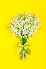 bouquet of lily of the valley flowers with a green bow on a yellow background top view close up