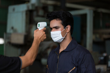 Factory worker using infrared forehead thermometer scan at head with male worker in front of the...