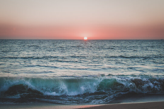 Sun setting in pink sky over Pacific Ocean as waves crash in Mexico