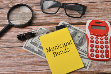 Top view of a banknotes, calculator, spectacles and magnifying glass with written Municipal Bonds on wooden background. Selective focus.