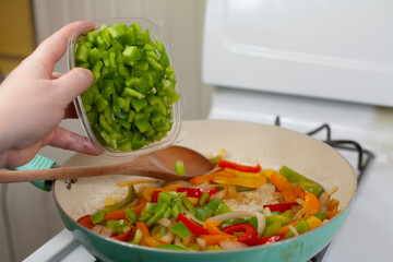 Green, Red and Pouring Green Bell Peppers into a Pan Filled with Red and Yellow Bell Peppers and White Onions