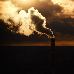 Silhouette of a chimney with white smoke coming over the city, evening sunset