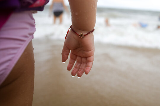 closeup of child hand dripping water at beach wearing bracelet