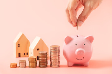 Hand putting a coin into pink piggy bank and stacking coin for saving concept on pink background,...