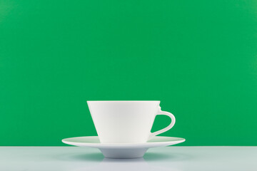 White tea cup against green background with copy space. Concept of green, organic or herbal tea, healthy life style and wellbeing
