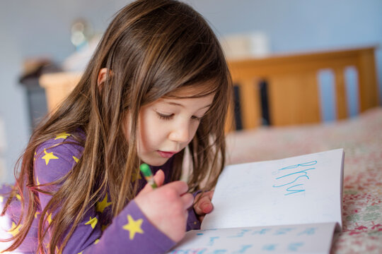 A focused little girl works quietly in her bed writing words in a book