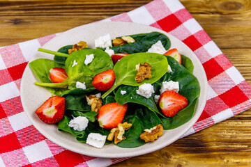 Fresh healthy salad with strawberry, spinach, walnuts and feta cheese on wooden table