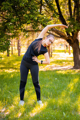 Healthy lifestyle concept. The girl is warming up in the park. Young fitness woman doing back and arm stretching getting ready for an evening workout in a summer park.