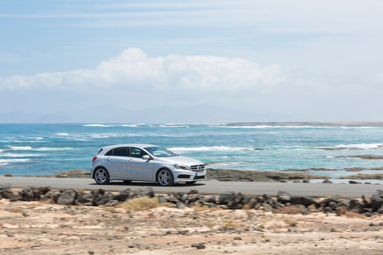 Grey car driving empty paved road with ocean in the background