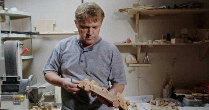 The senior carpenter of the tree master carefully examines the wooden typewriter, which he himself made in his workshop and thinks about how it can be improved and start a startup for business.